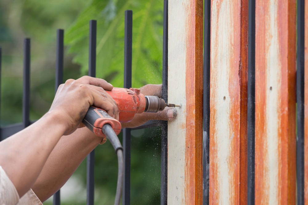 a man is drilling a hole in a fence with a drill .