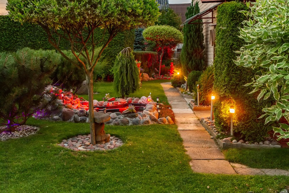 a lush green garden with a path leading to a house at night .