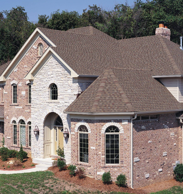 Two-story house with brick and stone exterior, brown roof, and arched windows.