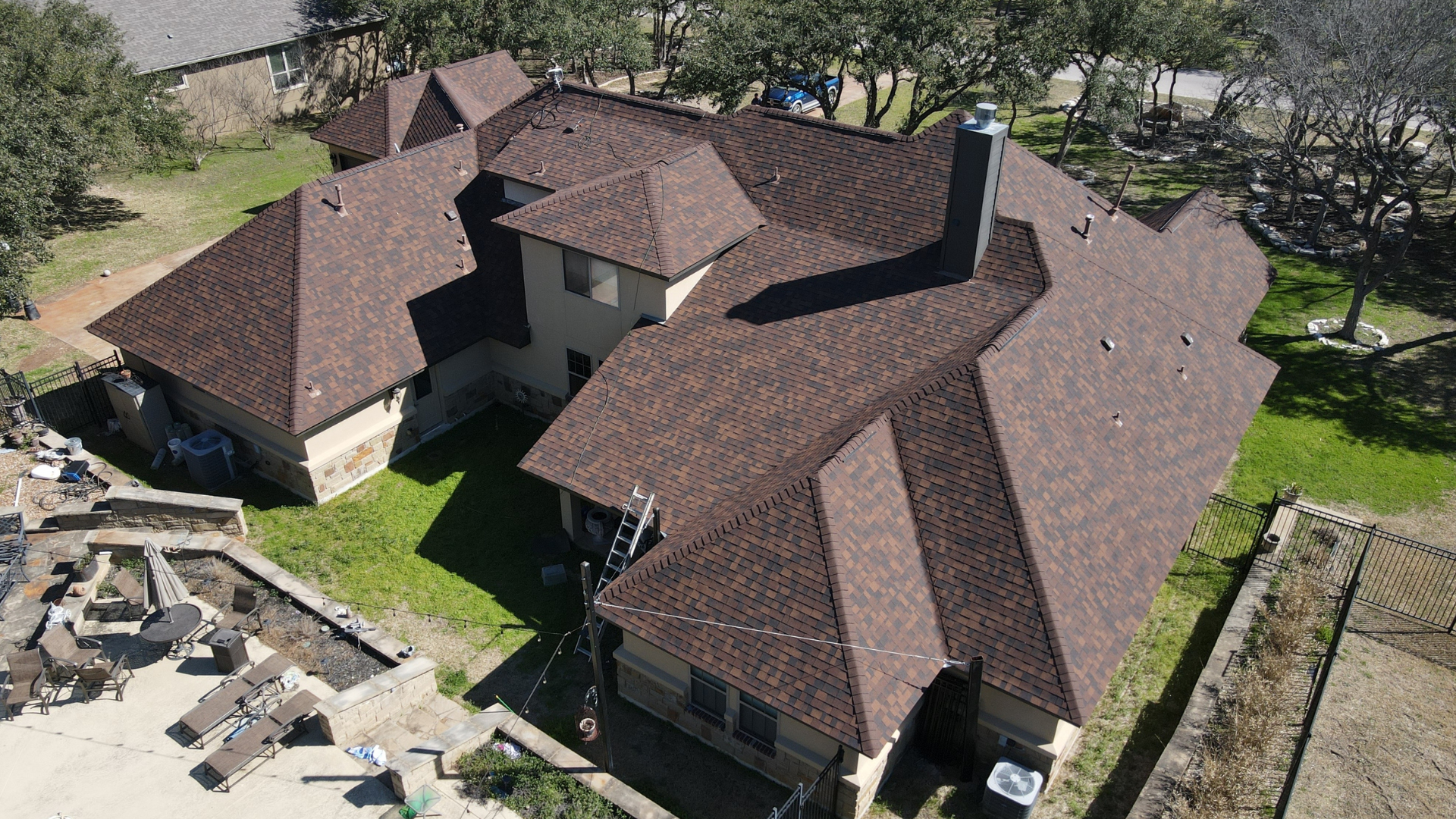 Aerial view of a large brown-roofed house on a green lawn with surrounding trees.