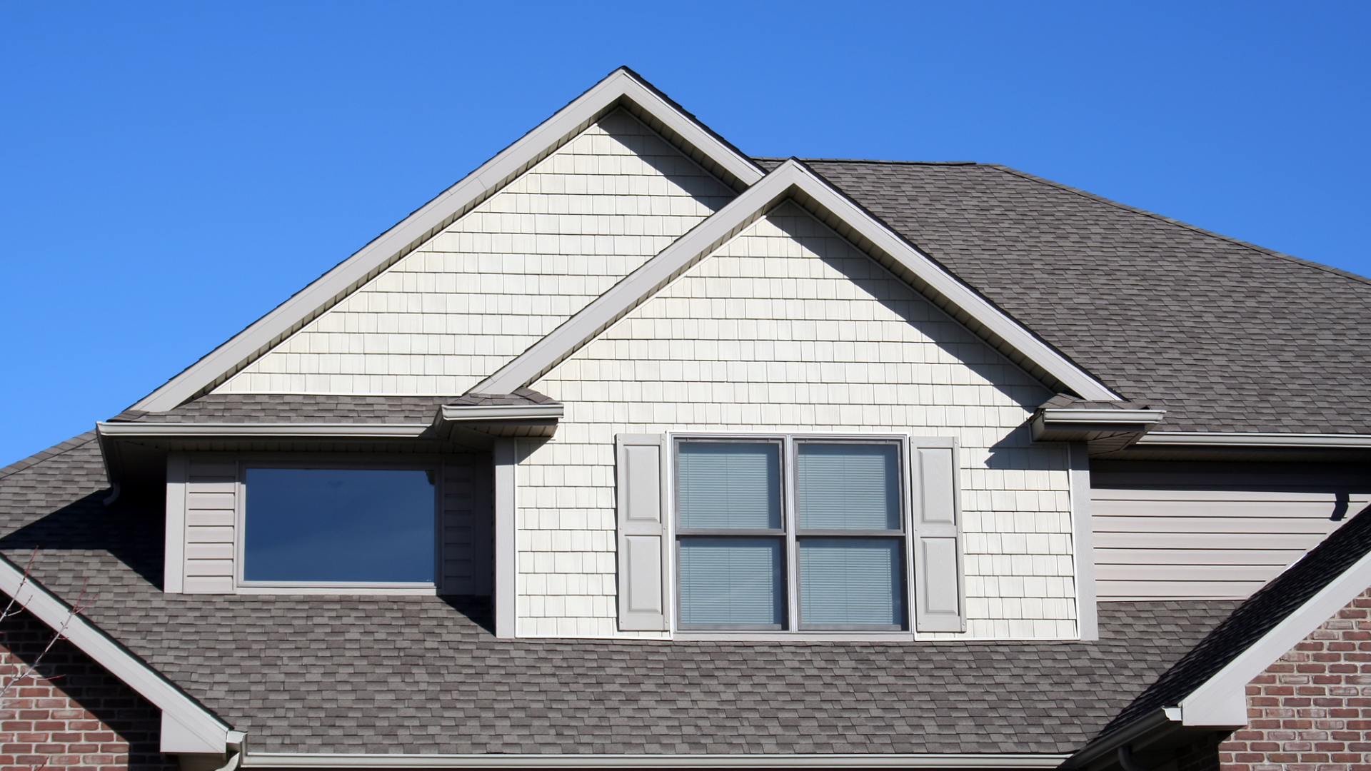 House roof with light-colored siding, two windows, and dark-colored shingles against a blue sky.