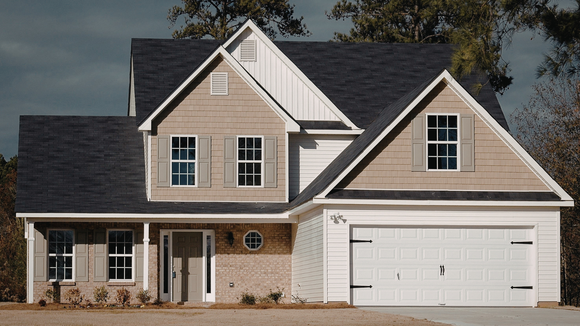 Two-story house with a white garage door, light brown siding, and dark gray roof.