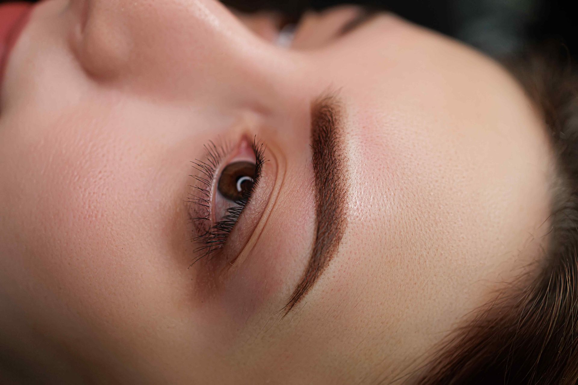 Close-up of a person's eye and eyebrow with permanent makeup. Brown eyebrow, light skin, and brown eye.