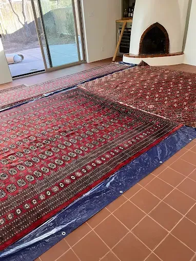Red oriental rugs laid out on a tile floor in a room with a fireplace and sliding glass door.
