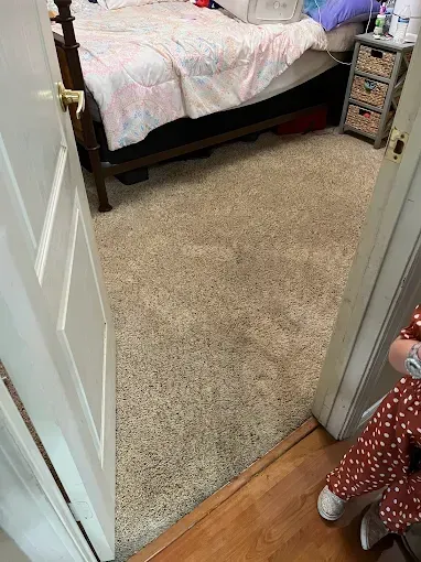 Bedroom doorway, carpeted floor, bed with bedding, person in the corner.