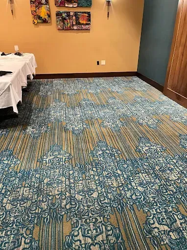 Room with patterned blue and tan carpet, tan walls, and a table with a white cloth.
