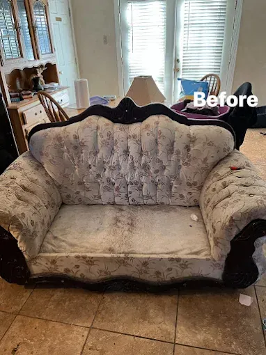 A worn, floral-patterned loveseat in a room, with visible stains. 