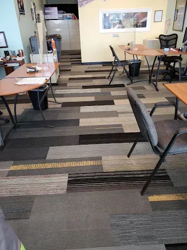 Office interior with tables, chairs, and patterned carpet in shades of gray, brown, and yellow.