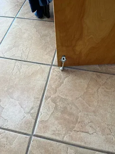 Cabinet door ajar with a chrome door stop on a tiled floor.