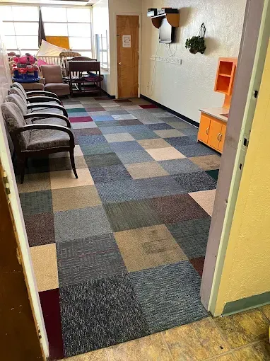 Waiting room with multi-colored square carpet, chairs, and play kitchen.