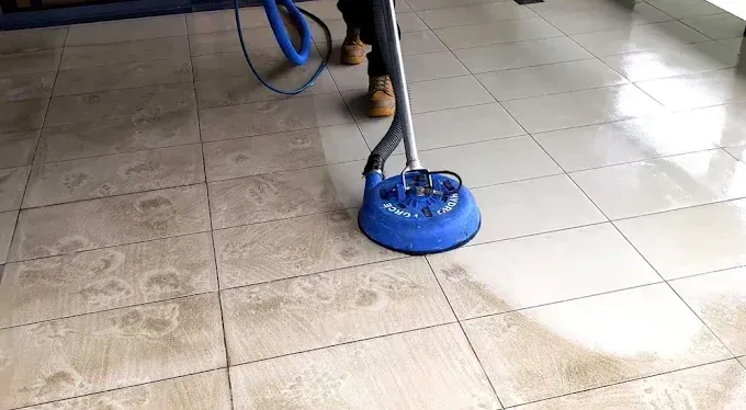 A person cleaning dirty tile floor with a blue circular cleaning machine.
