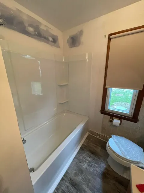 A bathroom with a tub , toilet and window.