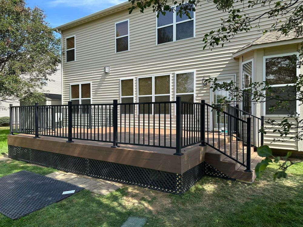 A large deck with a black railing in front of a house.