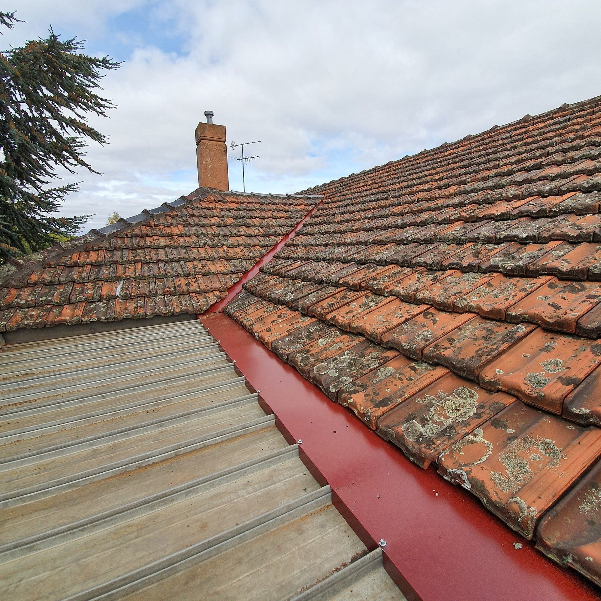 A tiled roof with a red gutter and a chimney in the background