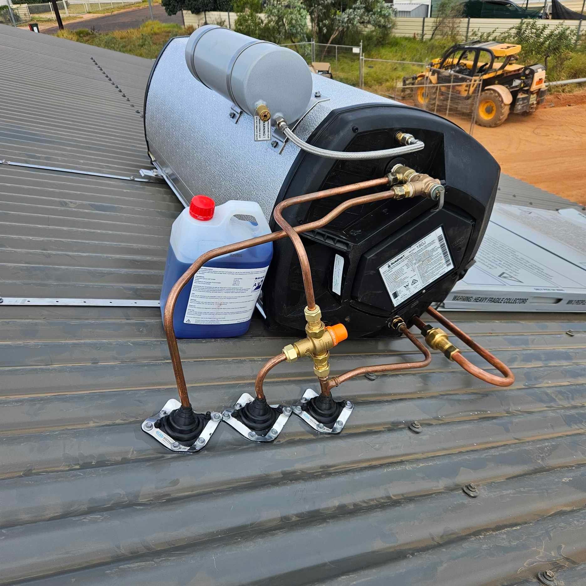 A water heater is sitting on a roof next to a bottle of blue liquid