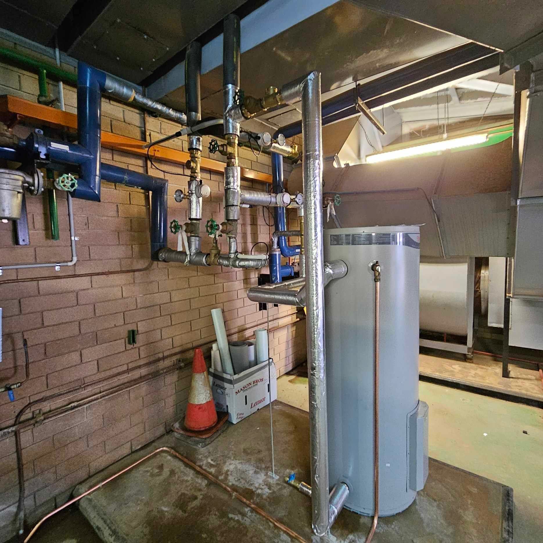 A large gray water heater is in a room with pipes