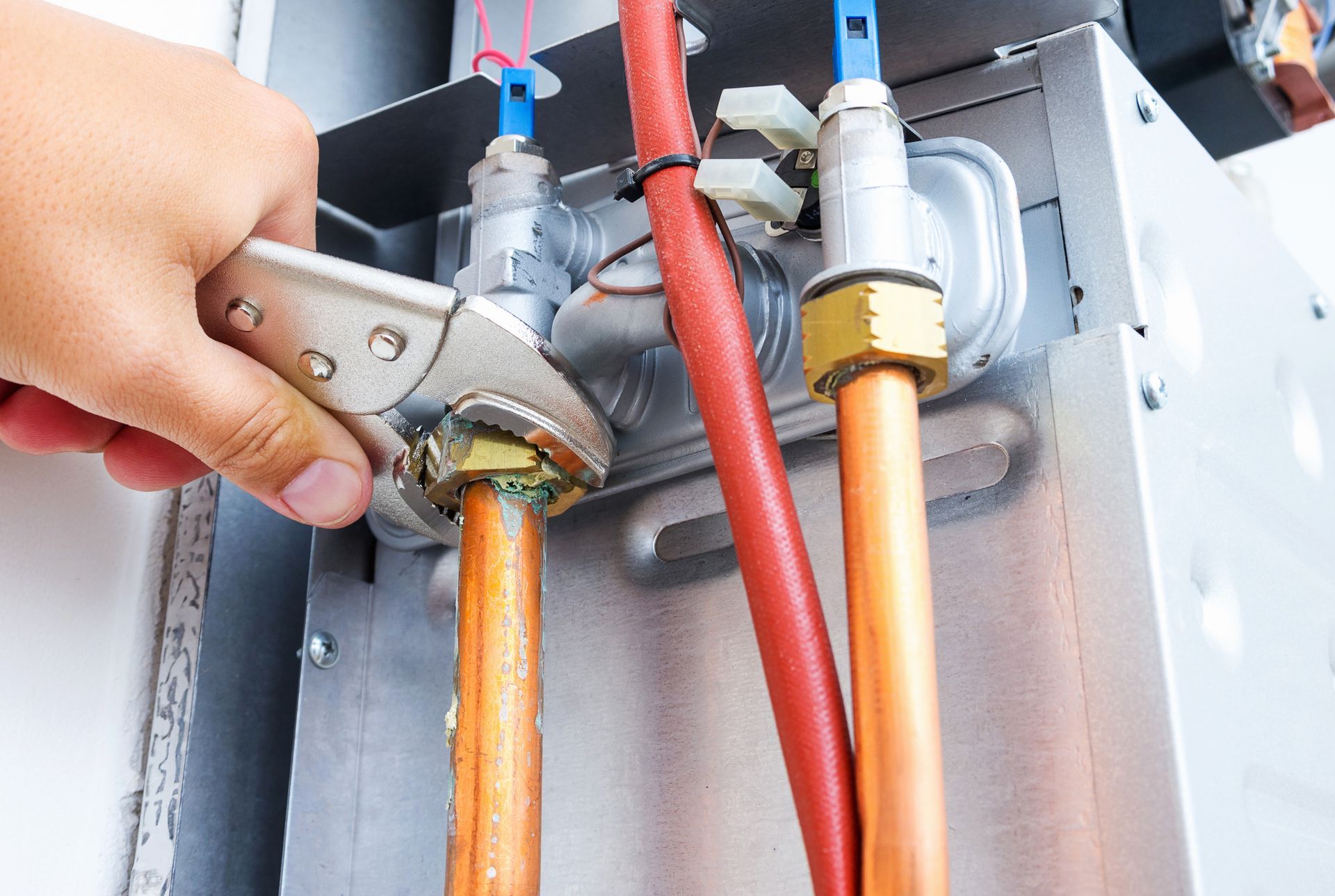 Hand using a wrench to tighten copper gas pipes connected to a metal appliance unit.