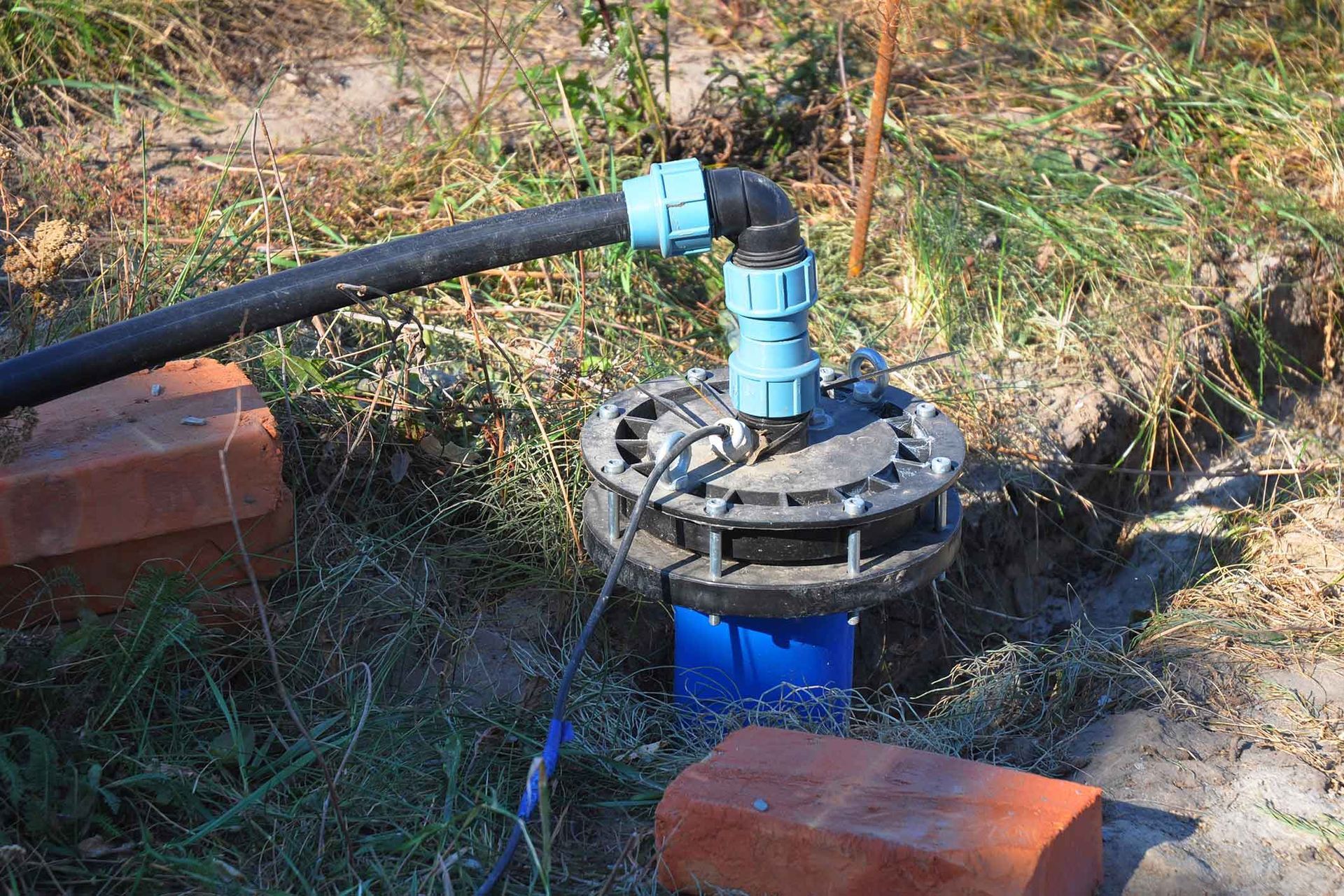 A water pump is sitting in the grass next to a brick wall.