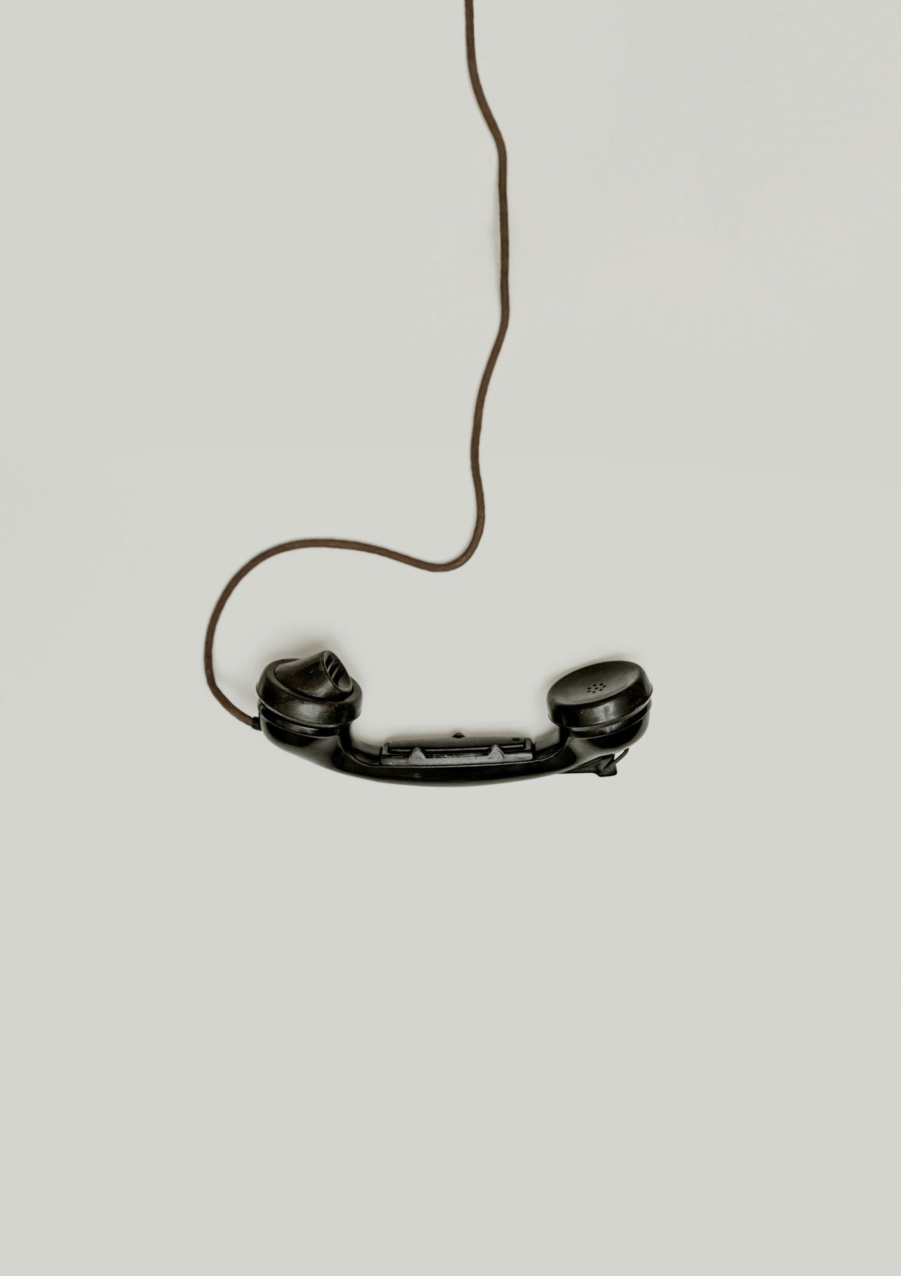 A black telephone is hanging from a wire on a white background.