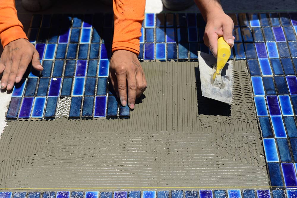 Workers Are Installing Porcelain Tiles In The Pool — Pool Maintenance in Airlie Beach, QLD