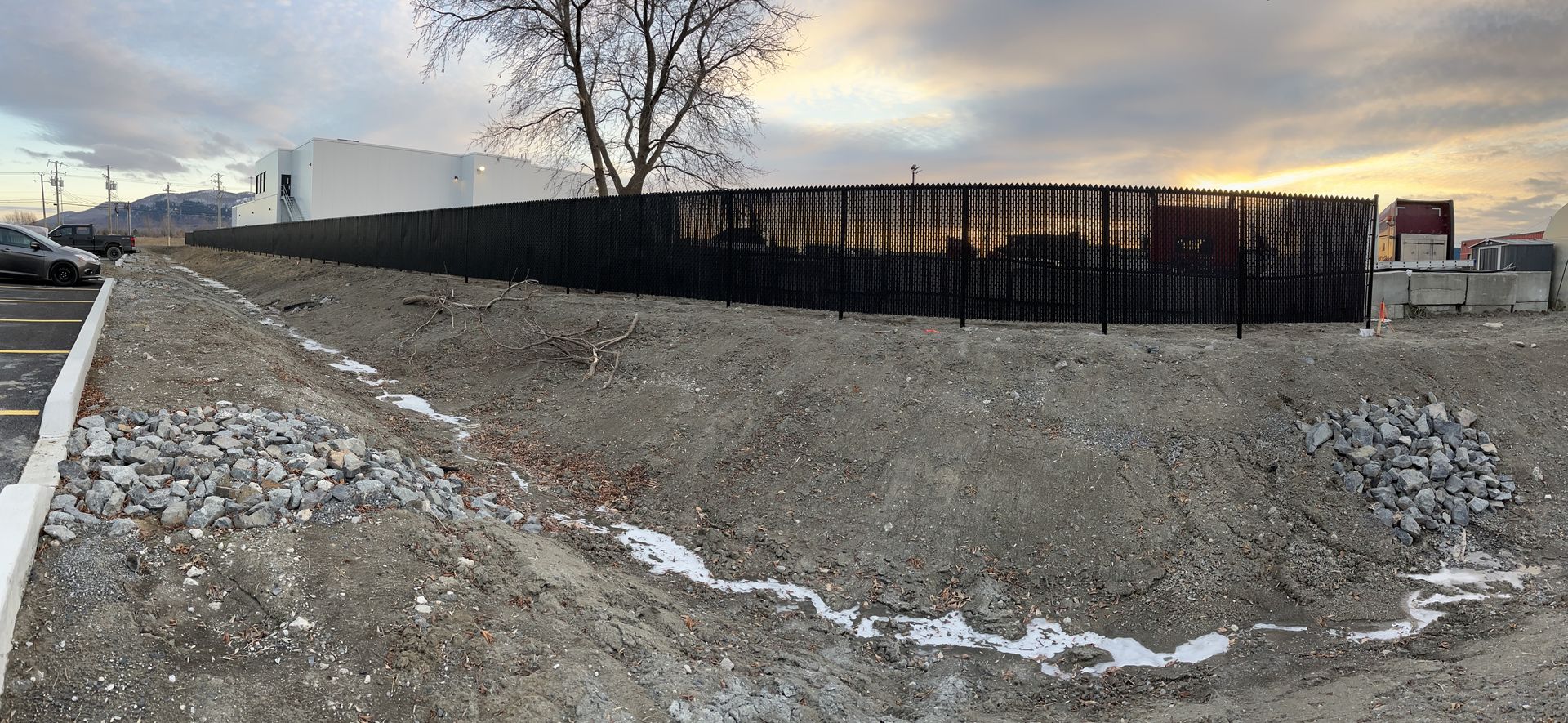 Une clôture entoure une zone de gravier avec un arbre en arrière-plan.