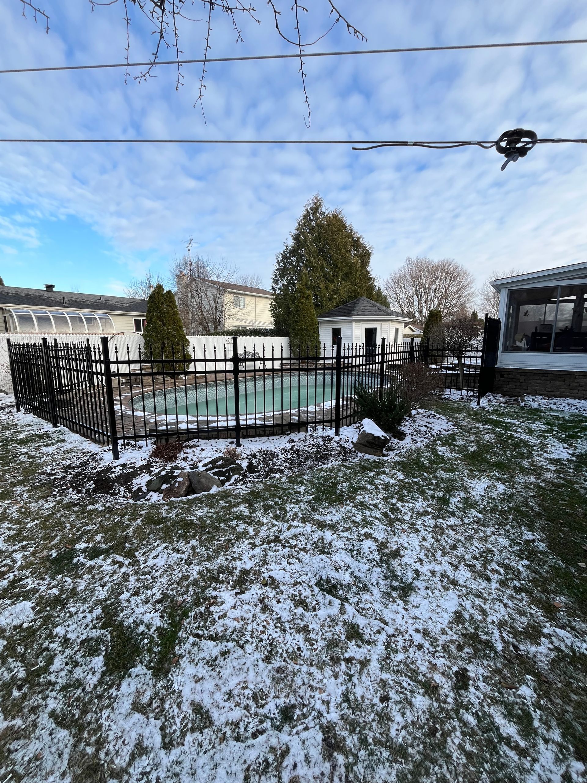 Une cour enneigée avec une clôture et une piscine en arrière-plan
