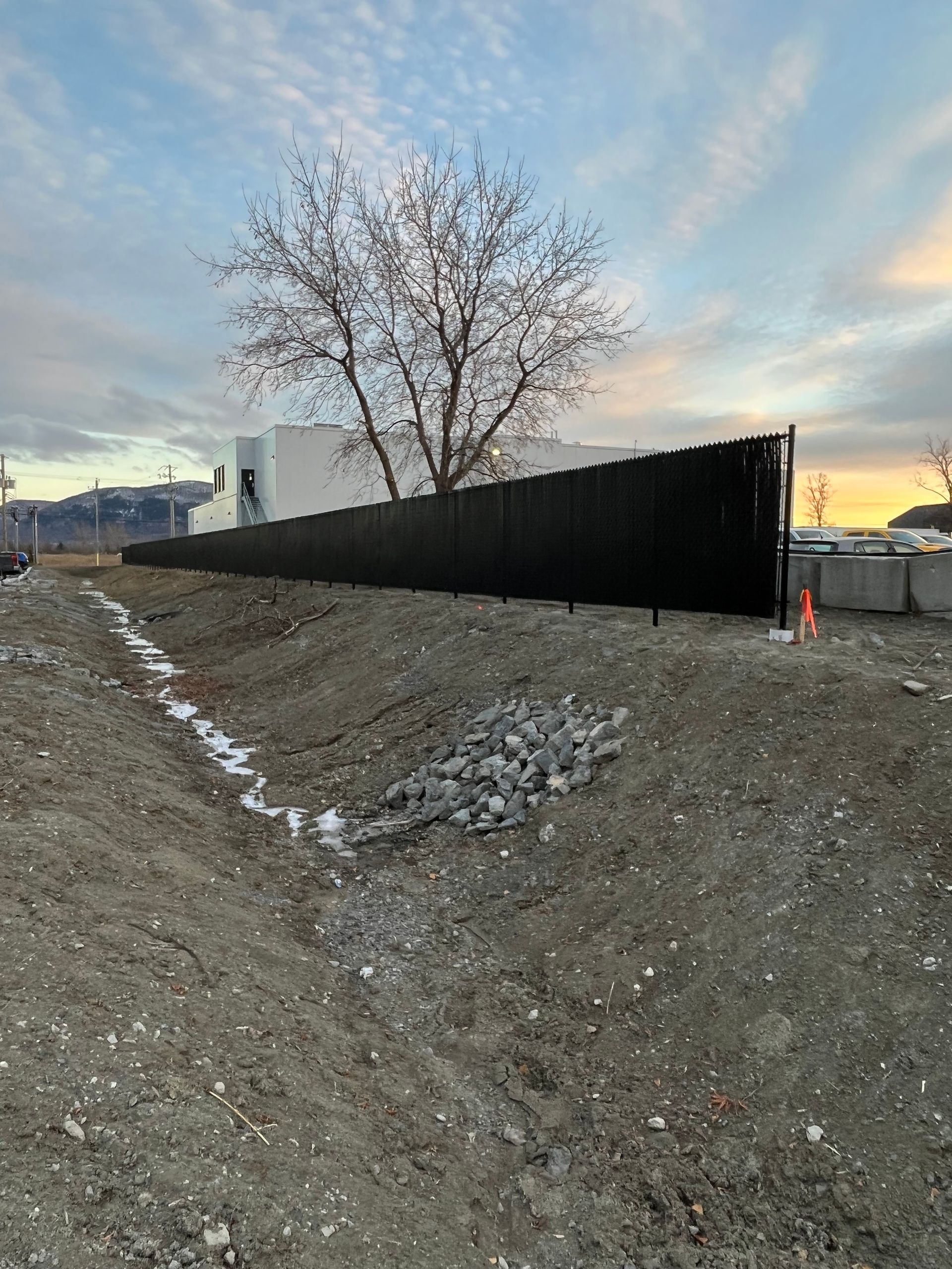Une grande clôture noire entoure un champ de terre avec un arbre en arrière-plan.