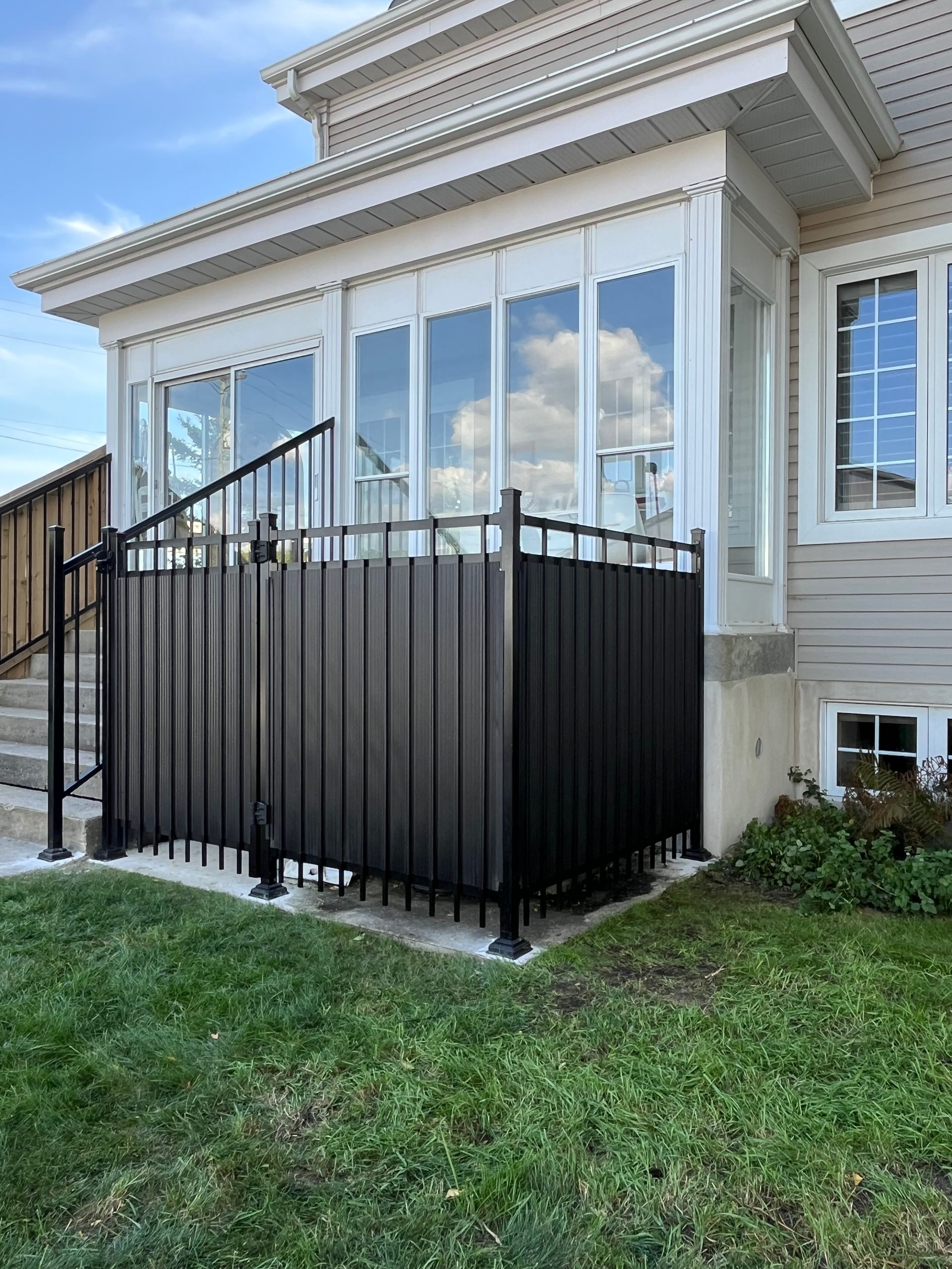 Une véranda avec une clôture noire et des escaliers devant une maison.