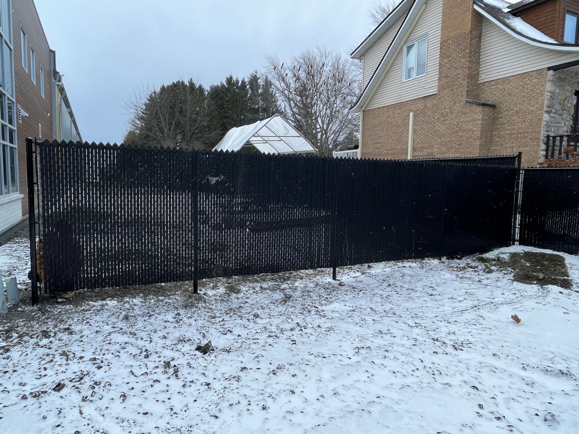 Une clôture noire entoure une cour enneigée devant une maison.