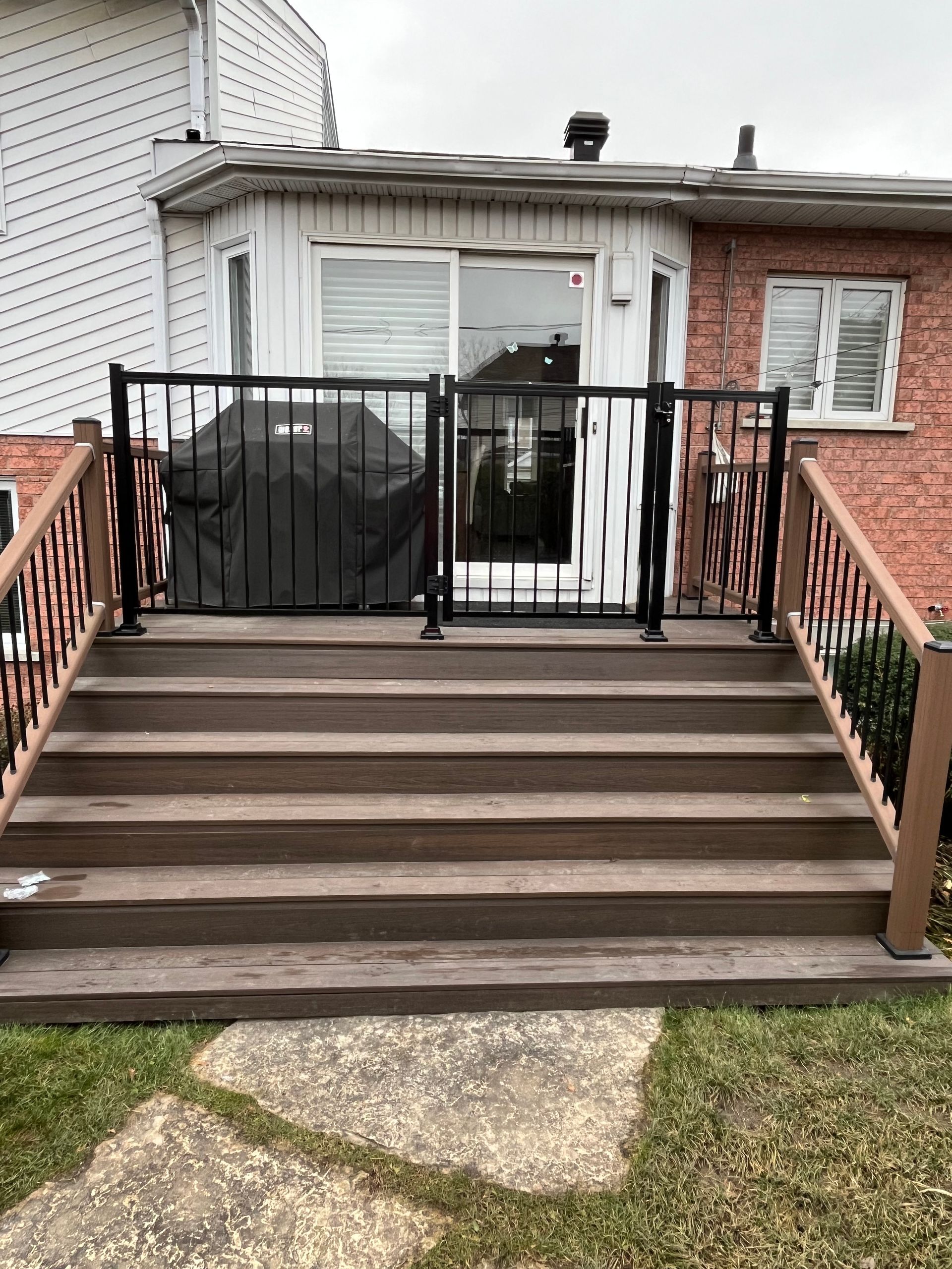 Une terrasse en bois avec des escaliers menant à une maison en briques.