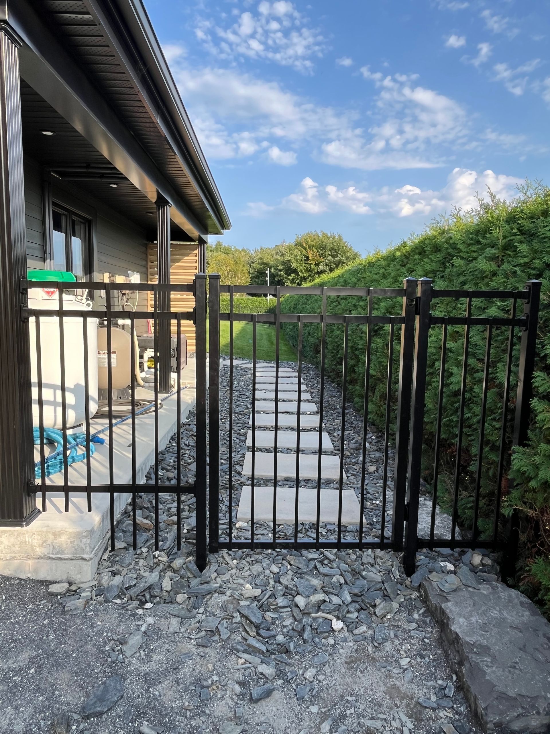Une clôture noire entoure un chemin de gravier menant à une maison.