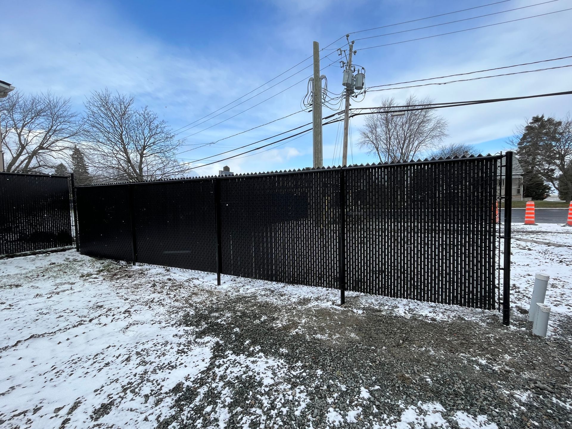 Une clôture grillagée noire est entourée de neige et de terre.