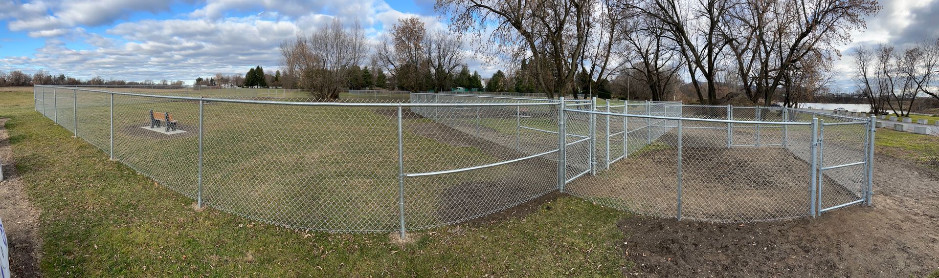 Une clôture grillagée entoure un champ herbeux avec des arbres en arrière-plan.