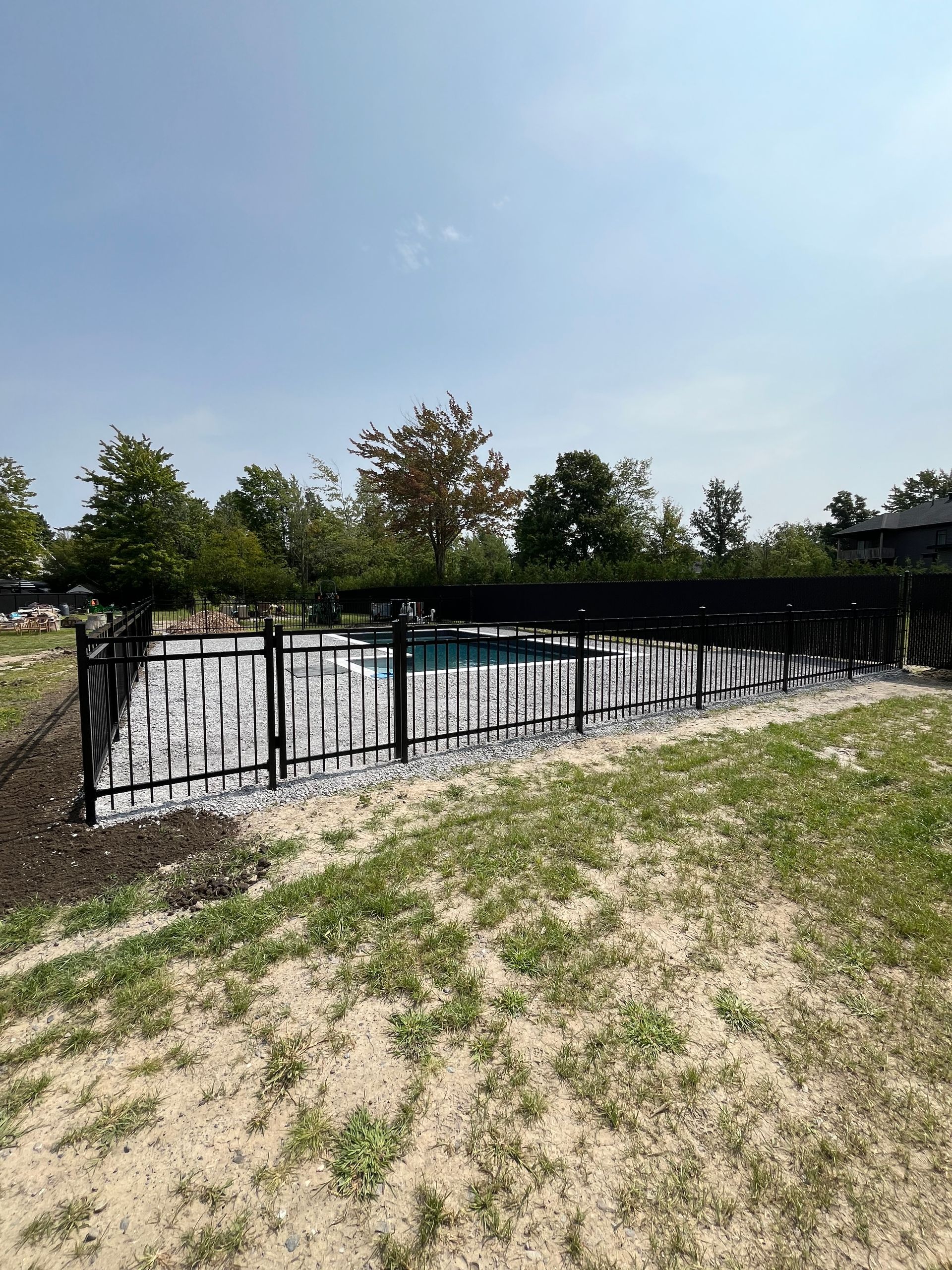 Une clôture noire entoure une piscine dans une cour arrière.