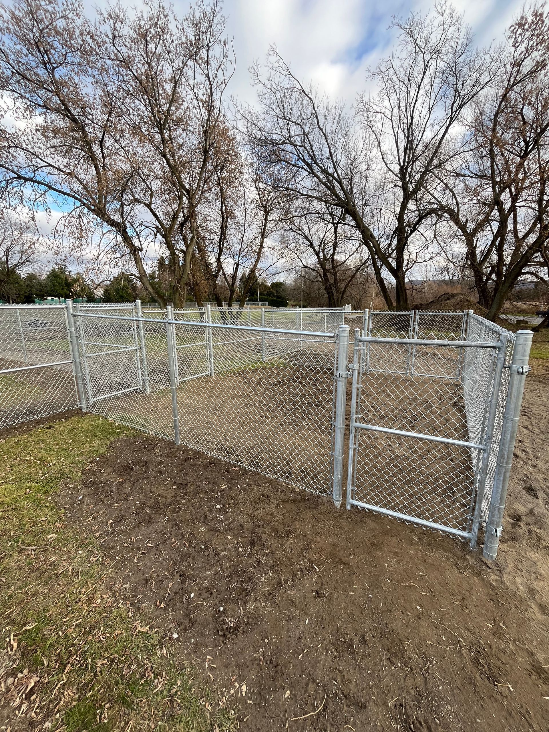 Une clôture grillagée avec une porte au milieu d'un champ de terre.