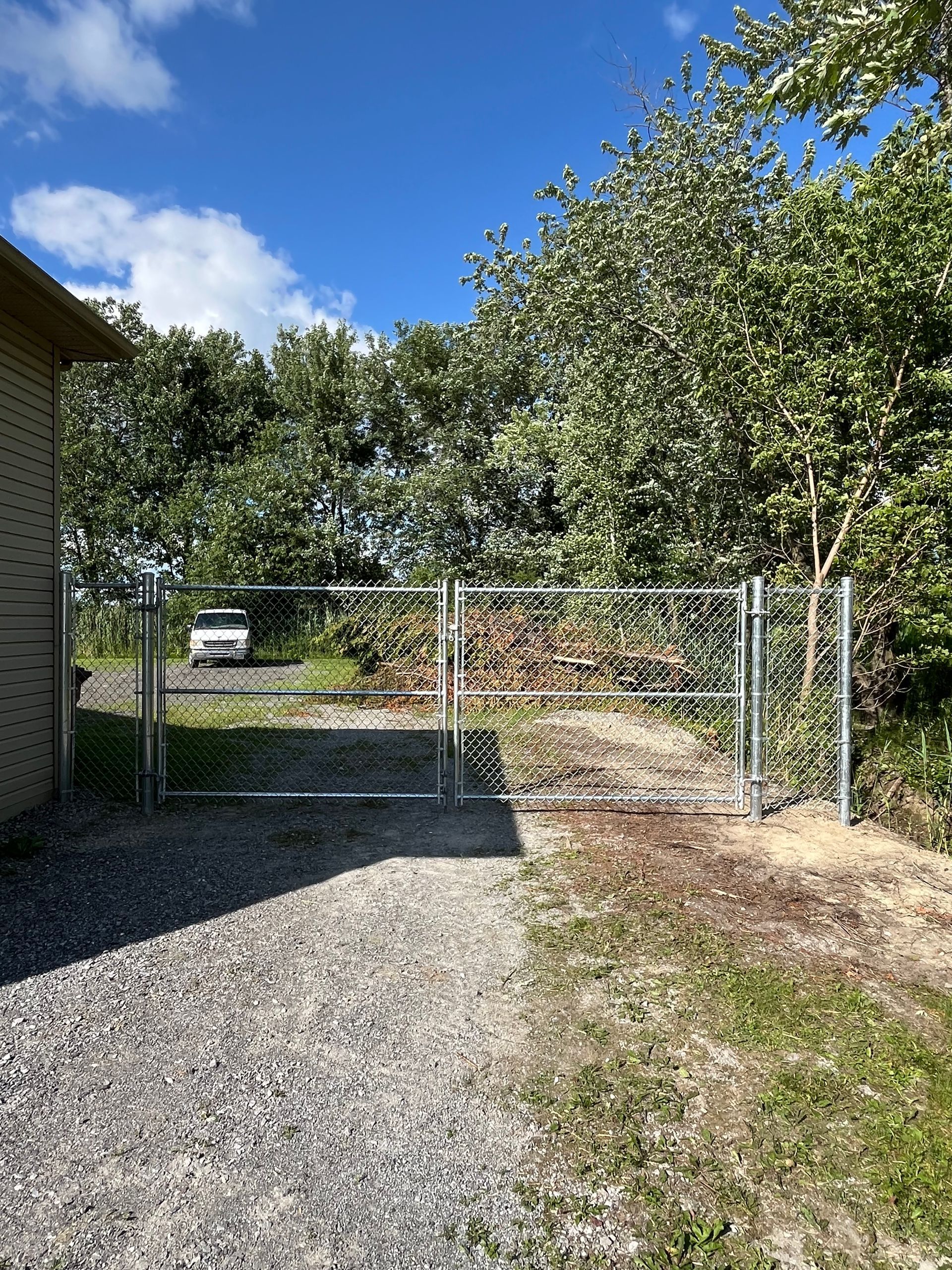 Une clôture grillagée entoure une allée de gravier menant à une maison.