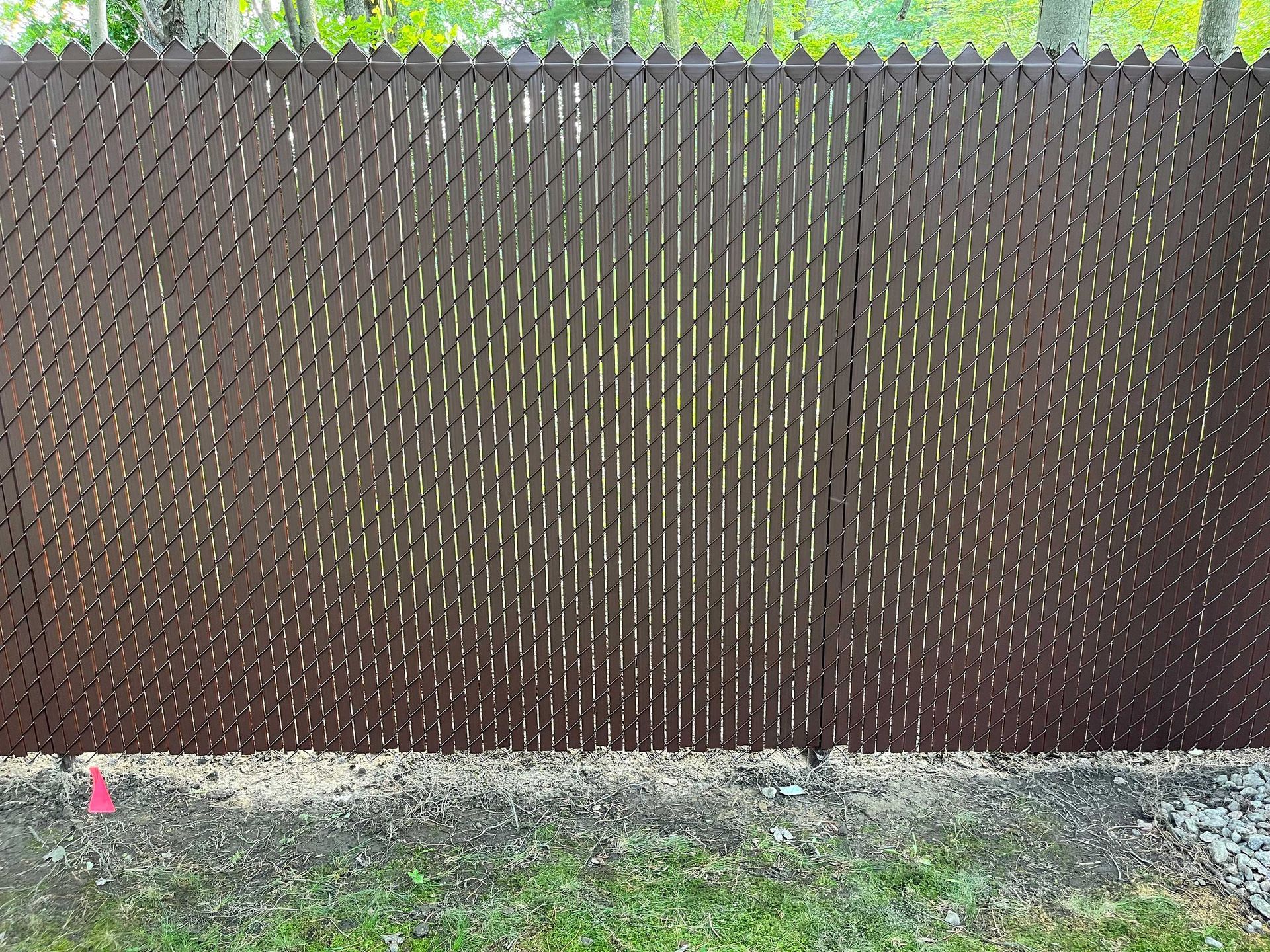 Une clôture grillagée marron se trouve au sommet d'un champ vert luxuriant.