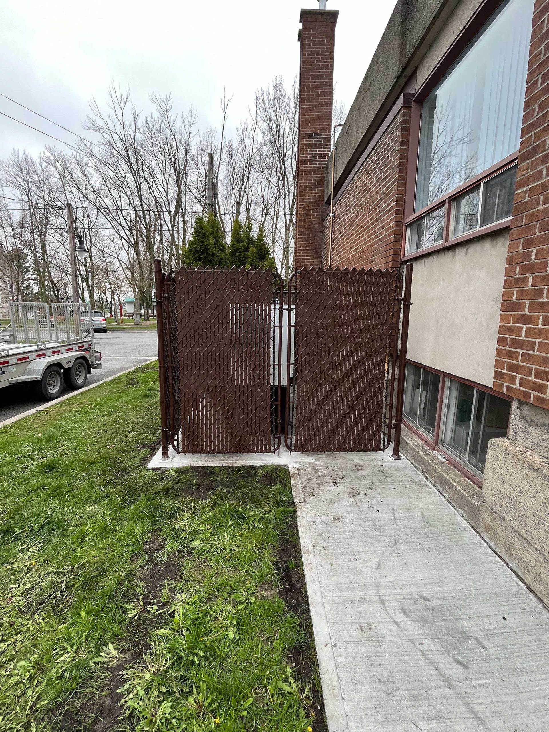 Un bâtiment en briques avec une clôture et un trottoir devant.