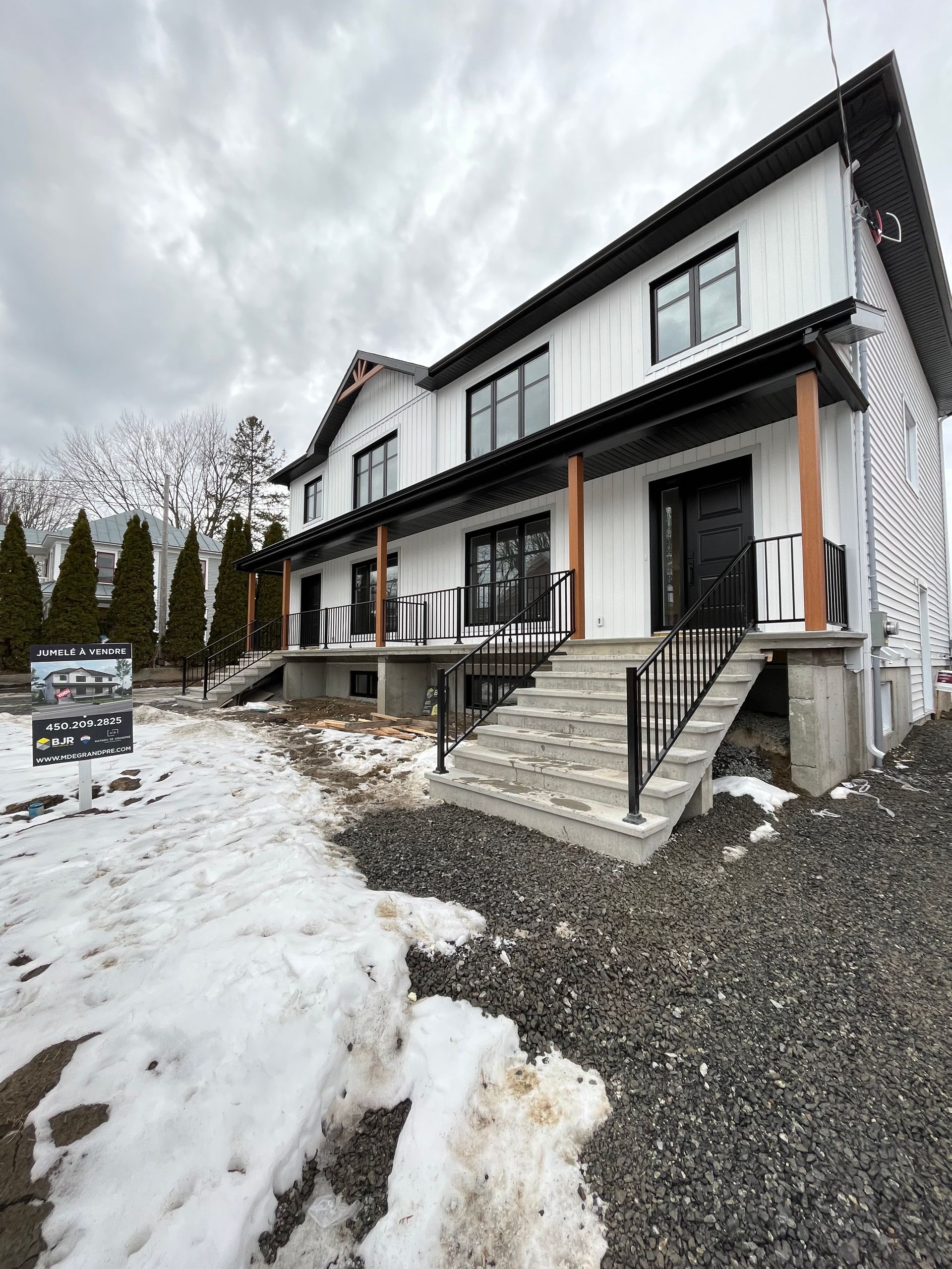 Une grande maison blanche avec des escaliers qui y mènent est entourée de neige et de gravier.