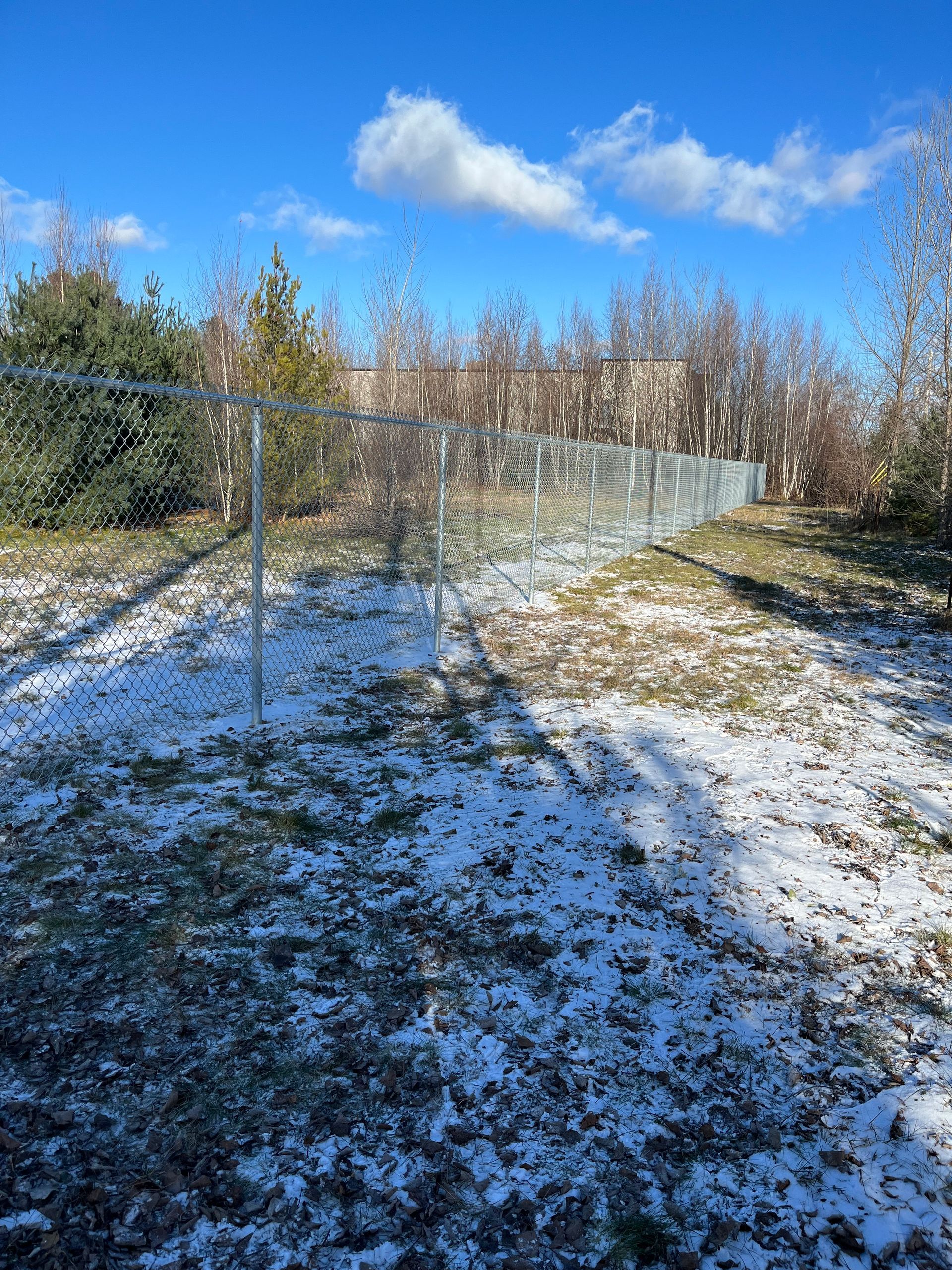 Une clôture grillagée entoure un champ enneigé avec des arbres en arrière-plan.