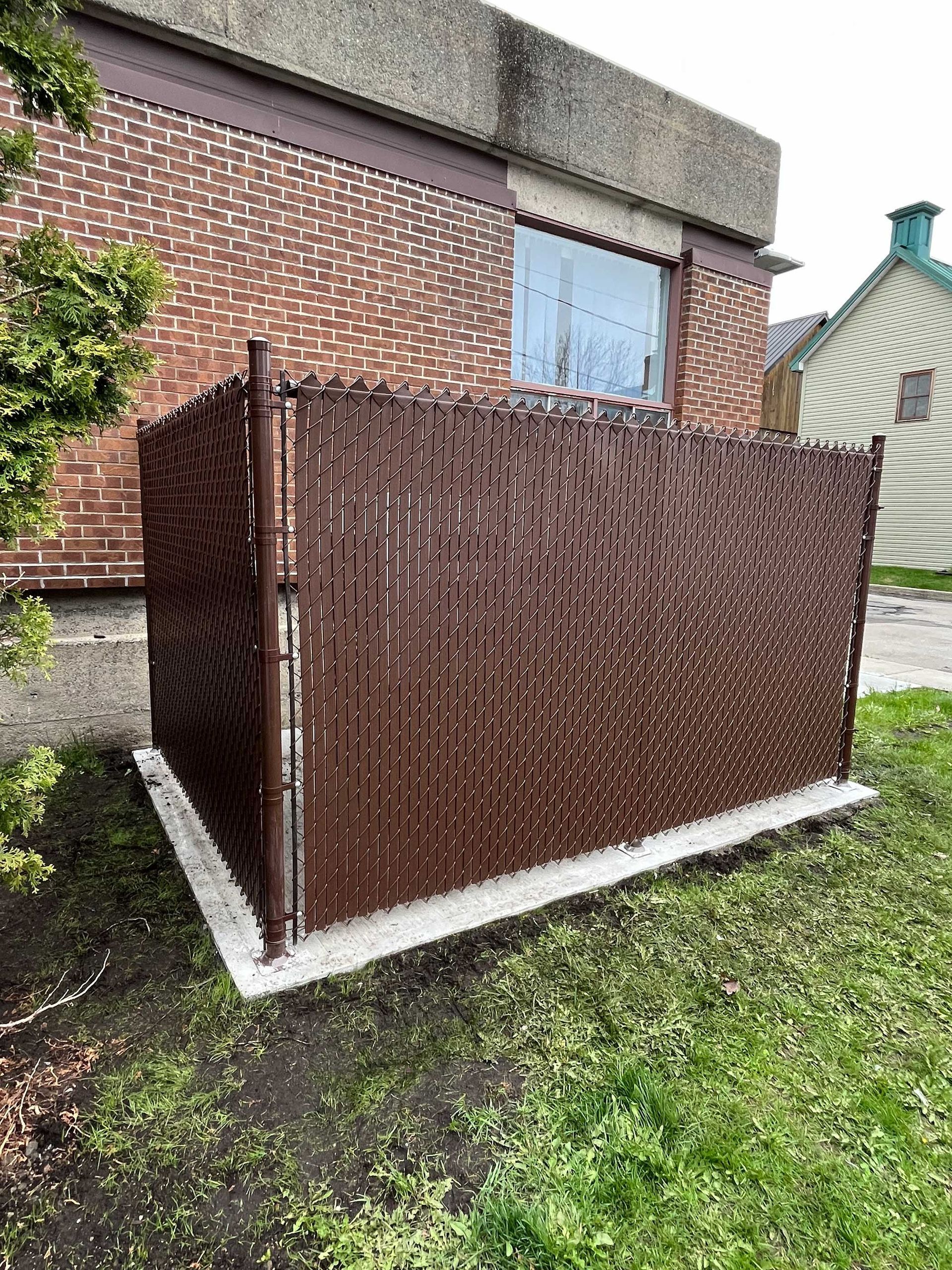 Une clôture grillagée marron se trouve devant un bâtiment en briques.