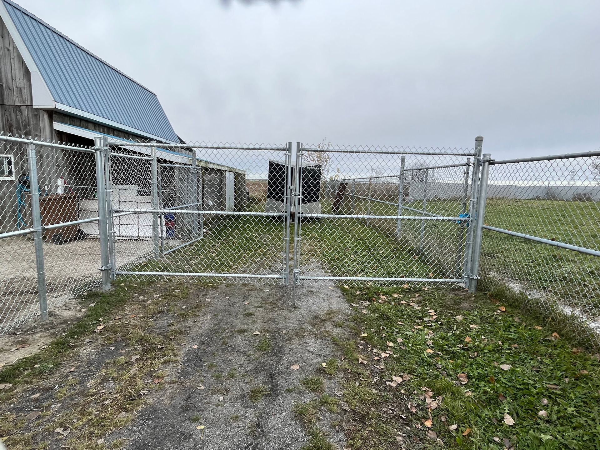 Une clôture grillagée entoure un chemin de terre devant une grange.