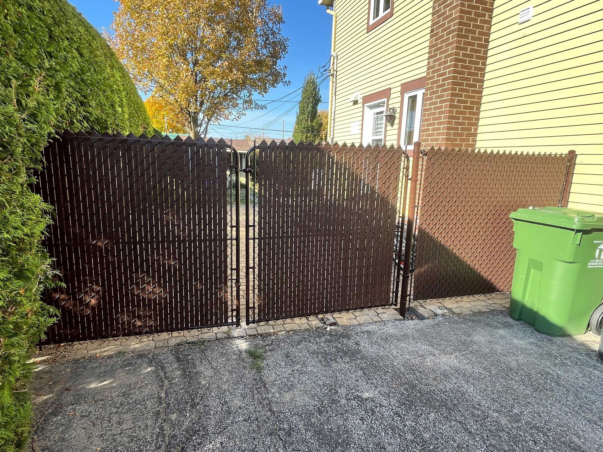 Une clôture grillagée noire entoure une allée de gravier devant une maison.