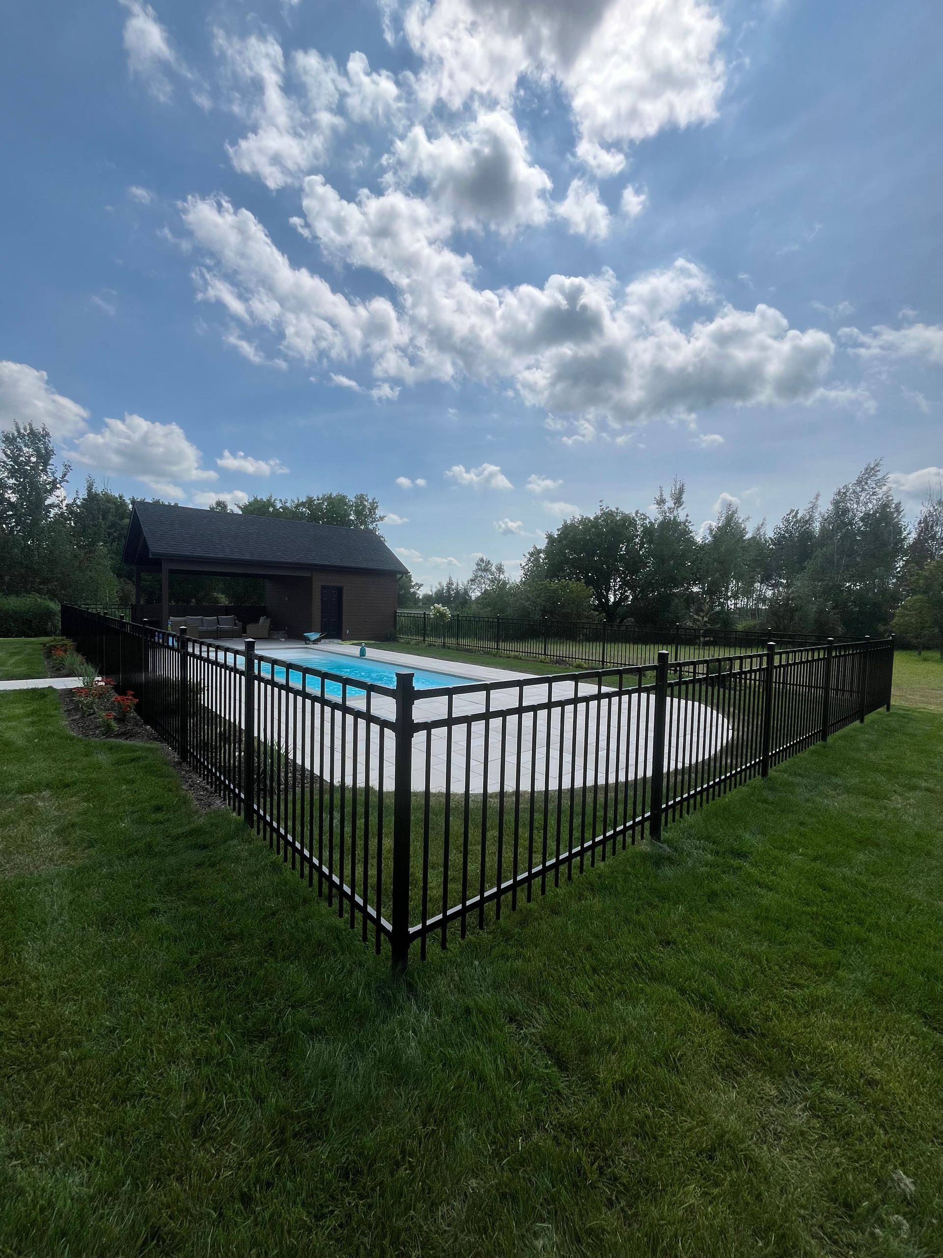 Une clôture noire entoure une piscine dans une cour arrière.