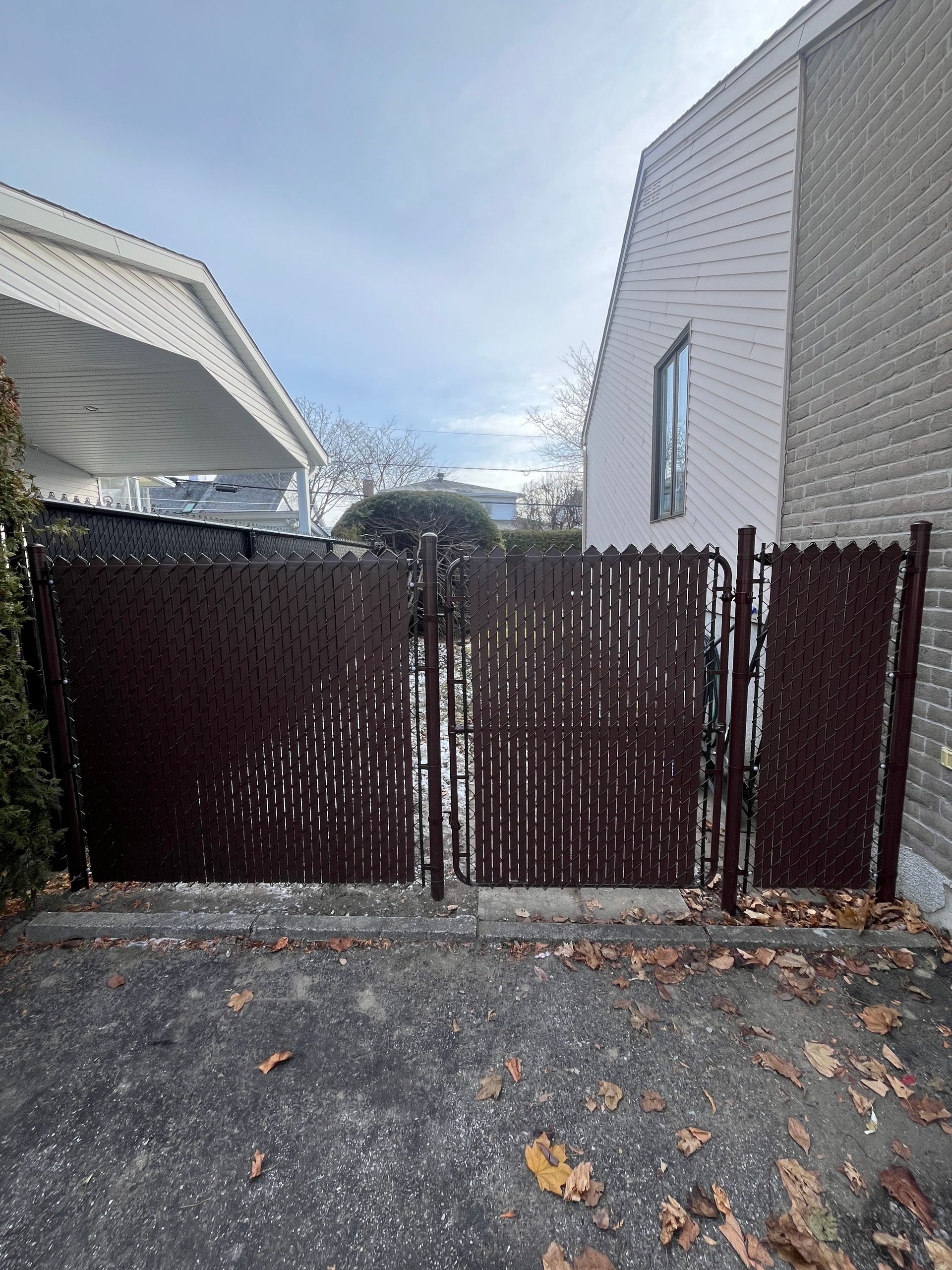 Une clôture grillagée marron entoure une allée devant une maison.