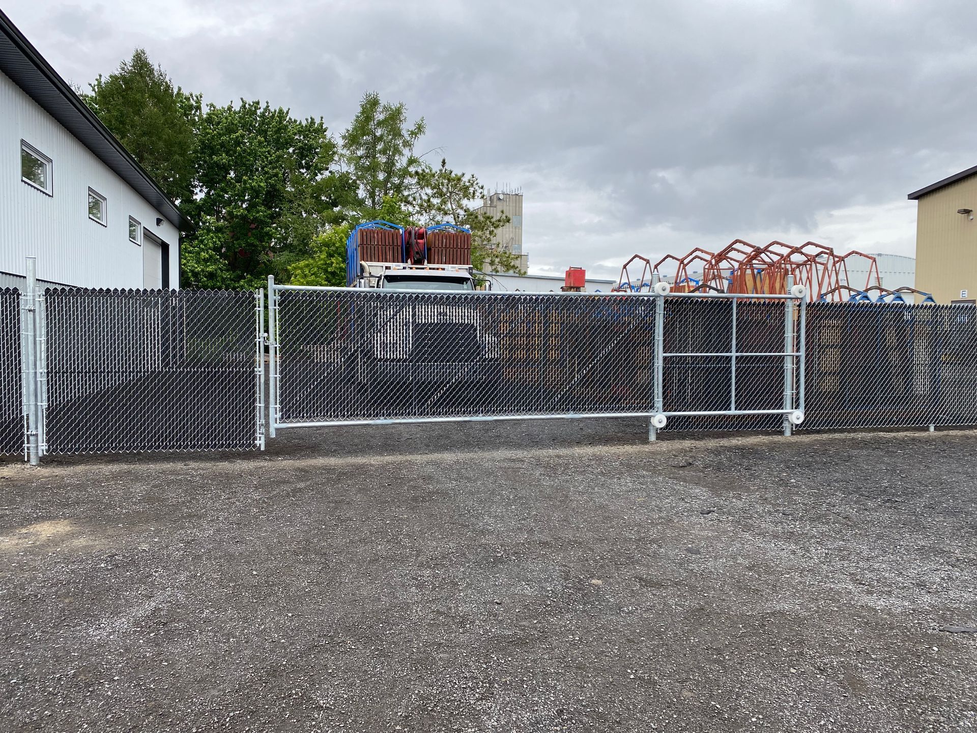 Une clôture grillagée entoure un terrain en gravier devant un bâtiment.
