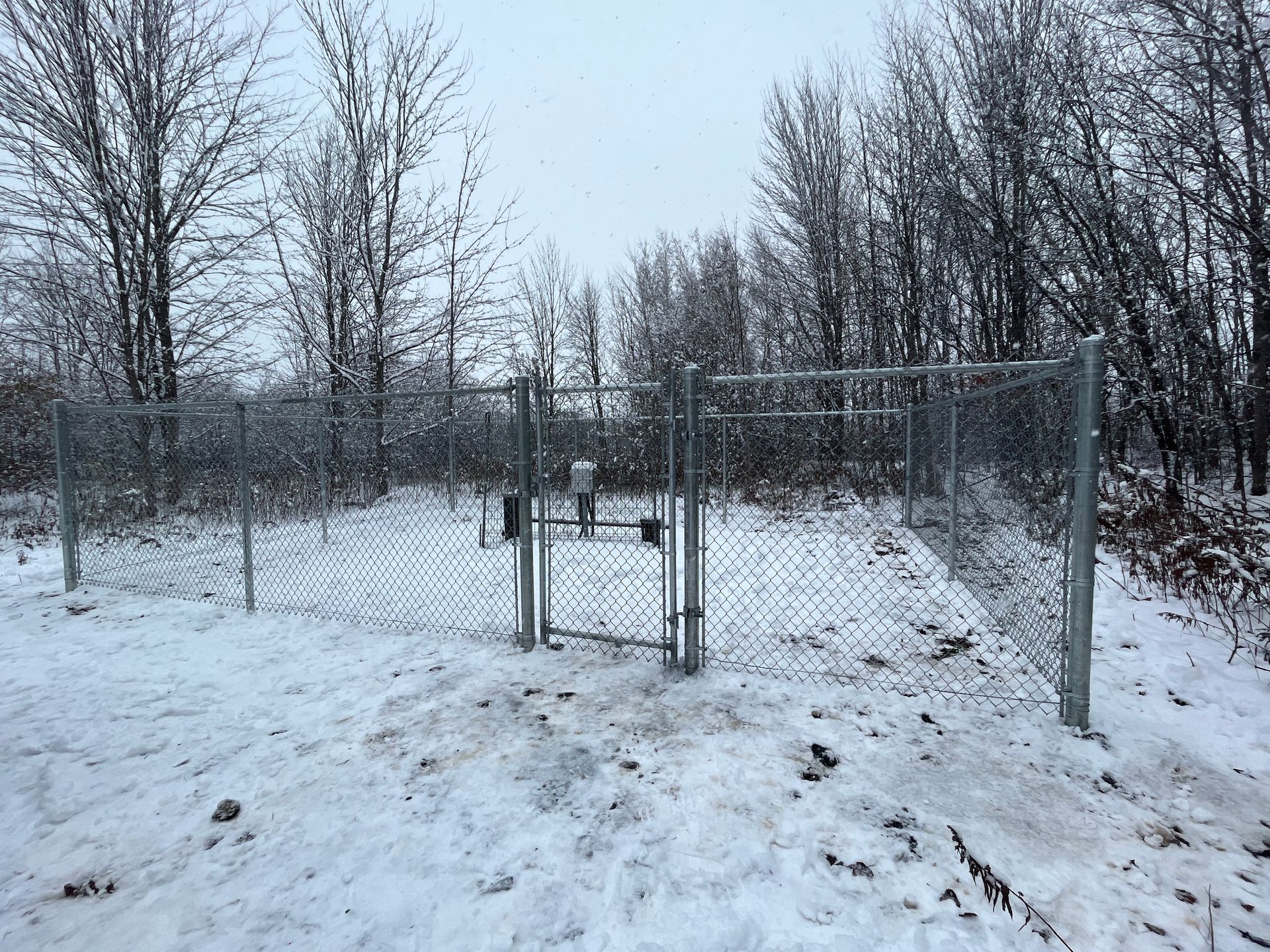 Une clôture grillagée est entourée de neige et d'arbres.
