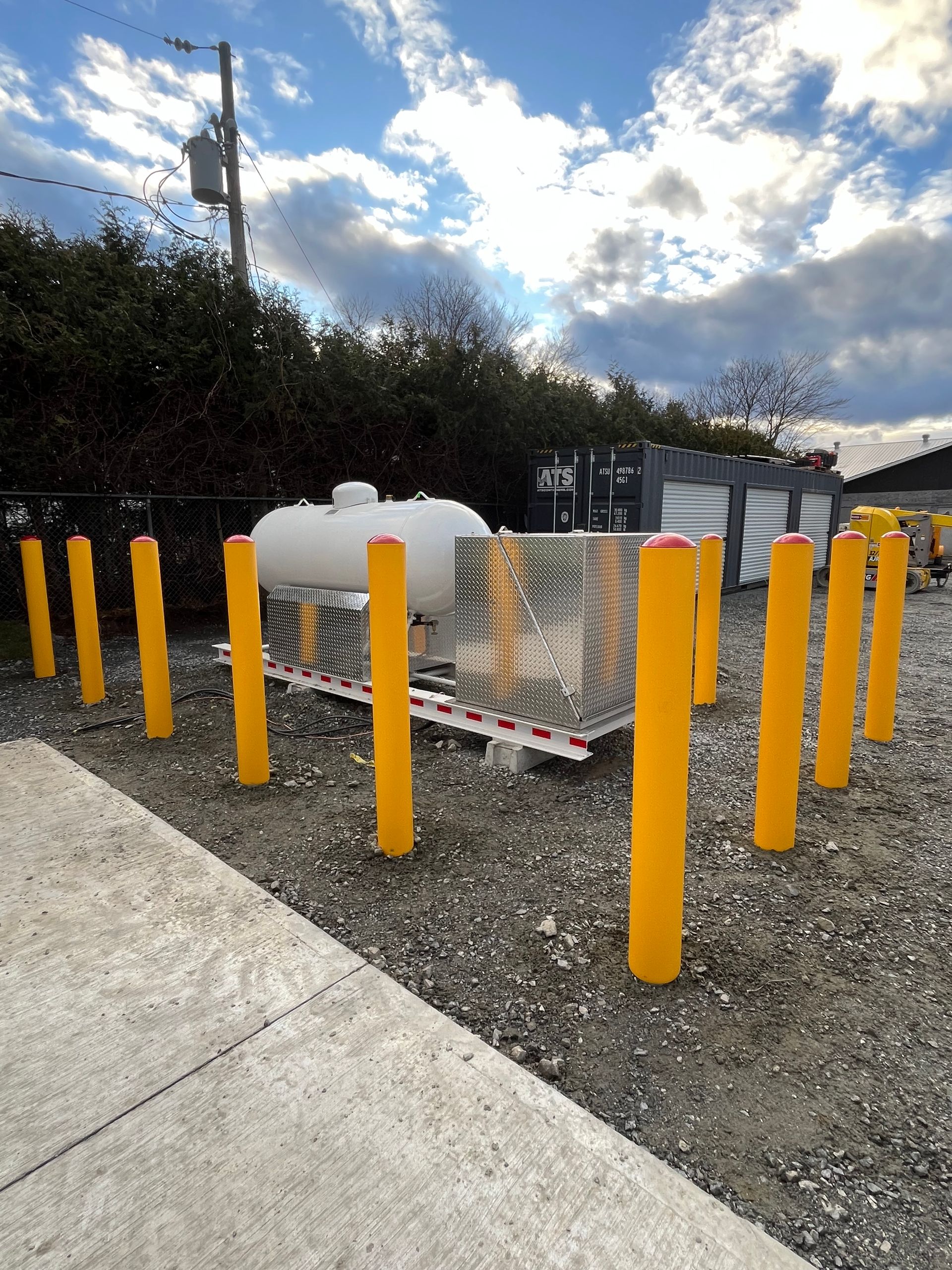 Un réservoir de propane est entouré de poteaux jaunes dans un parking.