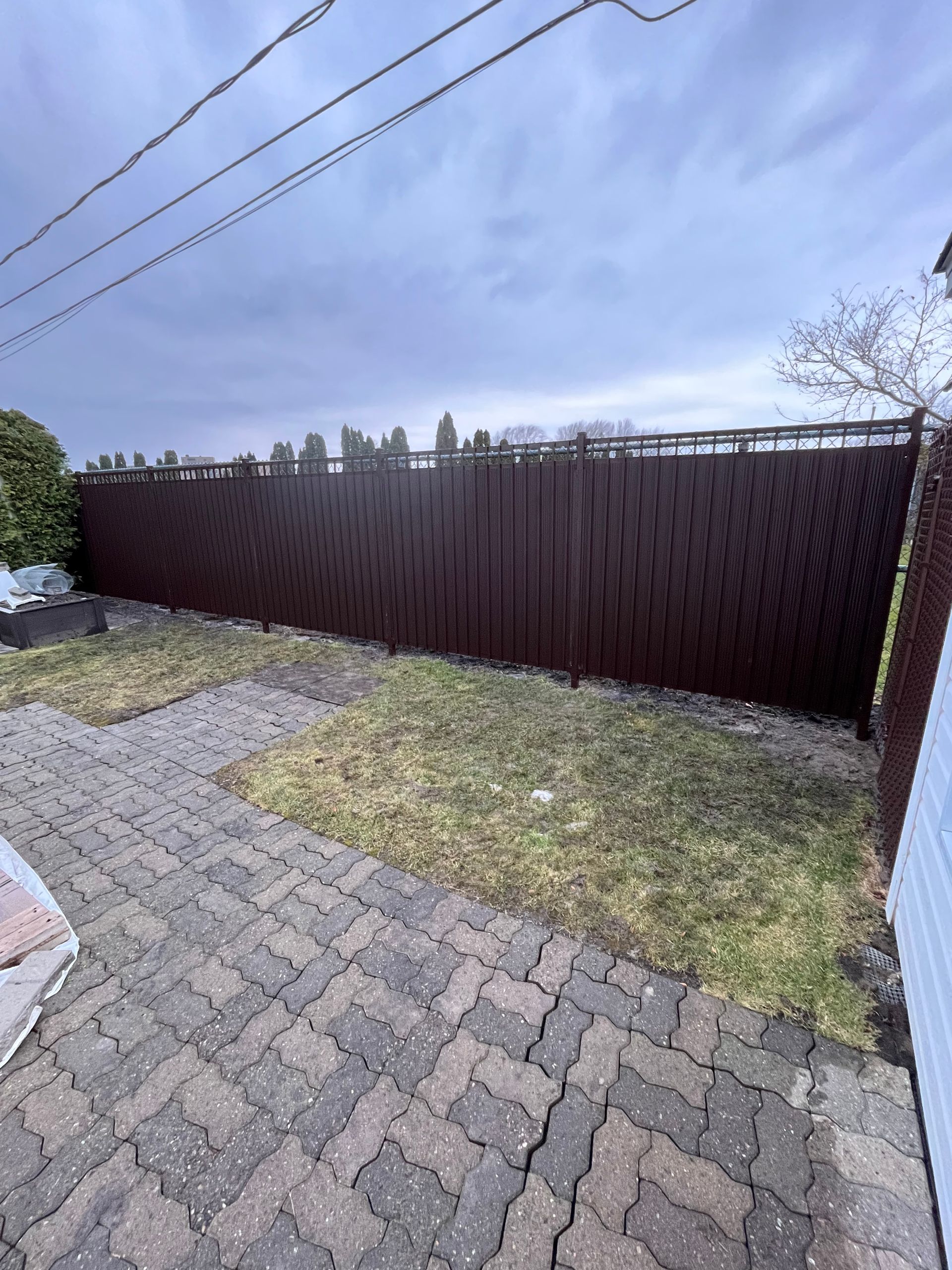 Une clôture brune est entourée d'herbe et d'une allée en briques.