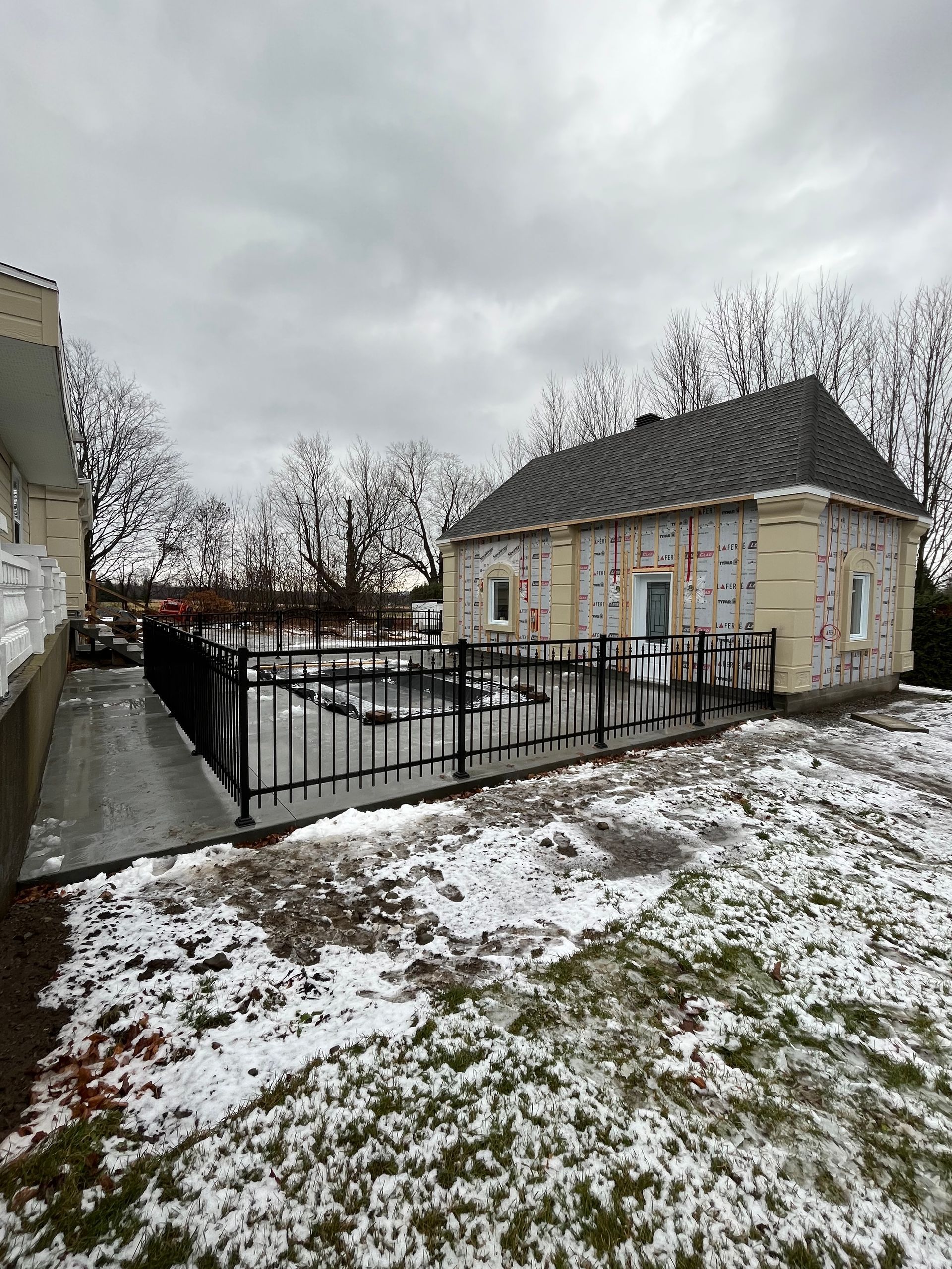 Une petite maison avec une clôture devant elle est entourée de neige.